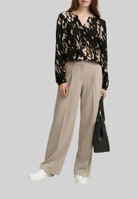Blouse noire avec un motif abstrait beige, pantalon beige à jambes larges, baskets blanches et sac fourre-tout noir. Tissu lisse avec une coupe décontractée.