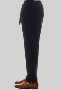 Pantaloni neri larghi con vita regolabile e tasche laterali. Il materiale sembra leggero. Indossati con mocassini intrecciati marroni.