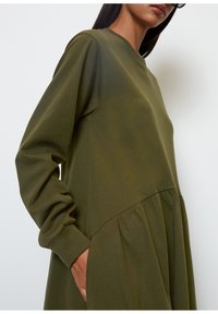 Zielona oliwkowa sukienka z miękkiego materiału, z długimi rękawami, okrągłym dekoltem i marszczoną spódnicą z bocznymi kieszeniami.