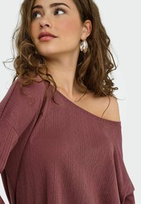 Top wine color con spalle scoperte, caratterizzato da motivi ondulati testurizzati e una vestibilità rilassata, realizzato in un materiale leggero e traspirante.