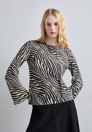 Long-sleeve top with a zebra-striped pattern in black and cream, featuring a rounded neckline and a relaxed fit. Textured fabric sits above a pleated skirt.