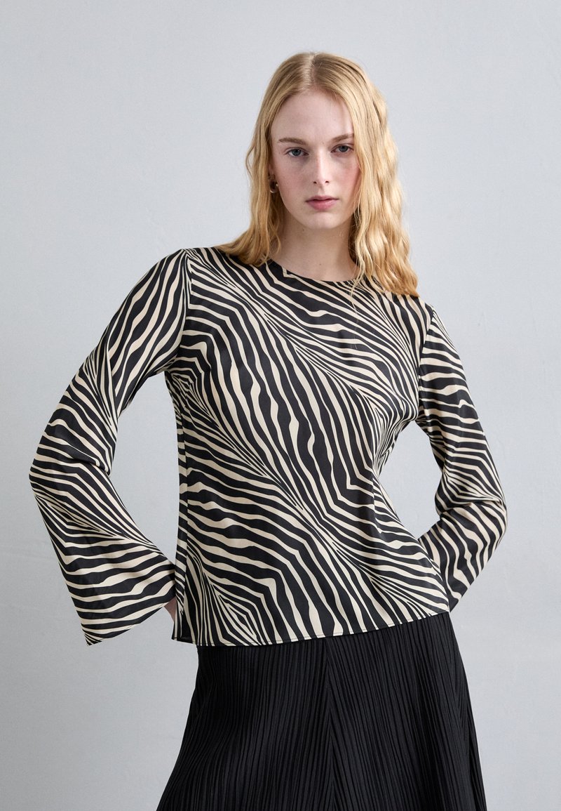 Long-sleeve top with a zebra-striped pattern in black and cream, featuring a rounded neckline and a relaxed fit. Textured fabric sits above a pleated skirt.