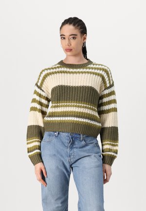 Dikke gebreide trui met horizontale olijfgroene, crème en witte strepen, ronde halslijn en geribde manchetten en zoom. Gecombineerd met blauwe jeans.