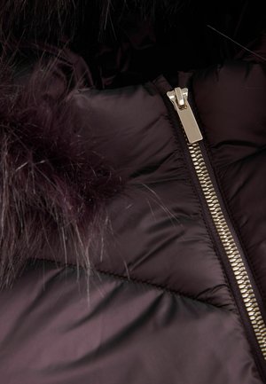 Donkerpaarse pufferjack met een glanzende afwerking, voorzien van een zilveren rits en een bontafwerking langs de capuchon. Textuurdetail van het stof is zichtbaar.