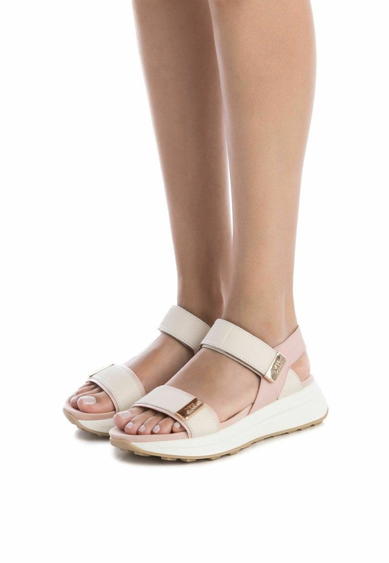 Sandalias ligeras con un esquema de colores en beige y rosa. Presentan correas anchas, un acabado texturizado y una suela blanca contrastante con agarre.