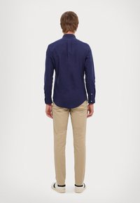 Navy blue long-sleeve shirt with a back yoke detail, paired with light beige trousers and casual shoes. Smooth fabric with fitted design.