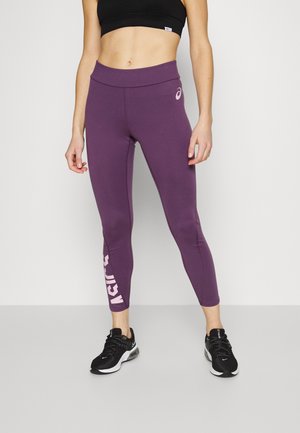 Leggings atletici viola con una texture liscia, vita alta e logo bianco a sinistra. Abbinati a sneaker nere.