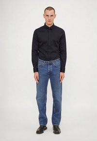 Tumši zils kreklbikses krekls, gaiši zili džinsa bikses, valkātas ar melniem ādas apaviem. Apģērba komplekts ir klasiskā piegriezuma ar vienkāršu dizainu.