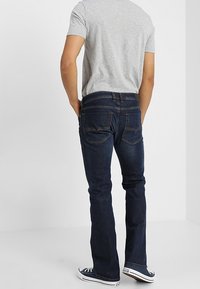 Jeans de mezclilla azul oscuro con un diseño de pierna recta, que cuentan con bolsillos traseros y una cintura de altura media, combinados con una camiseta gris de manga corta.