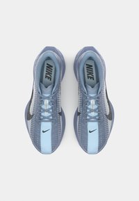 Nike running shoes with a mesh upper in light blue and grey, featuring a black swoosh, rounded toe, and textured detailing along the side.