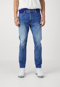 Blue denim jeans with a relaxed fit and a light wash; features a dark ribbed waistband and slightly distressed accents at the pockets.