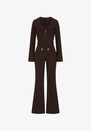 Brun jumpsuit med rund krave, lange ærmer og knaplukning foran. Har vide ben og dekorative knapper ved hoftelommer. Glat tekstur.