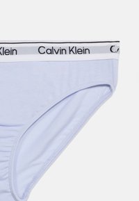 Ανοιχτό μωβ γυναικεία εσώρουχα σλιπ με λευκή ελαστική ζώνη μέσης που φέρει μαύρη επιγραφή «Calvin Klein».