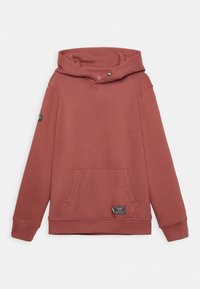 Sudadera de color óxido con bolsillo tipo canguro en el frente, mangas largas y pequeños parches de marca negros en el bolsillo y en el brazo izquierdo.