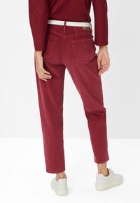 Pantaloni in corduroy rossi con una vestibilità dritta, dotati di due tasche posteriori e una cintura bianca. Indossati con sneakers chiare.