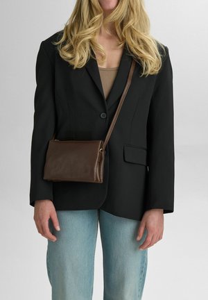 Ruskea nahkainen crossbody-laukku, jossa on sileä pinta ja läppädesign. Yhdistetty mustaan bleiseriin ja vaaleansinisempiin farkkuihin. Säädettävä hihna näkyvissä.