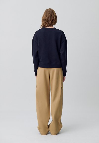 Sudadera de la marina con hombros caídos y tejido texturizado. Combinada con pantalones cargo de pierna ancha en marrón claro que cuentan con bolsillos laterales y un ajuste relajado.