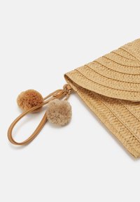 Clutch in paglia intrecciata beige con motivo a onde, dotata di due pom-pom morbidi in marrone chiaro e scuro, e una tracolla in pelle per il trasporto.