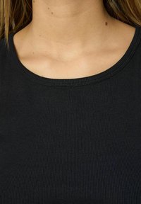 Top negro de canalé con un escote redondo, diseño ceñido y una tela suave y texturizada. La tela presenta detalles de canalé en horizontal.