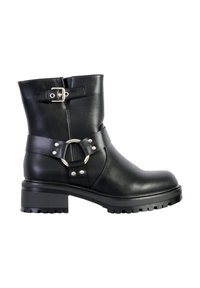 Black leather ankle boot featuring a round metallic buckle detail, harness strap with studs, and a chunky treaded sole.