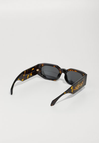 Black sunglasses with tortoiseshell pattern, angular shape, dark lenses, and gold "VERSACE" logo on the side.