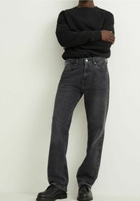 Sudadera negra combinada con jeans rectos de lavado oscuro y zapatos negros de suela gruesa. Tejido suave con un corte relajado y un diseño clásico.