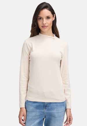 Light beige long-sleeve top made of soft fabric, featuring a high collar, subtle twist detail at the neckline, and a fitted silhouette.