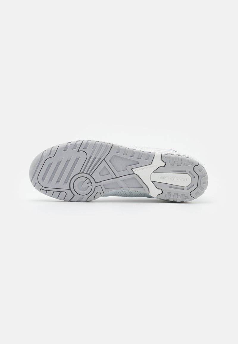 Semelle de chaussure de sport gris clair avec un caoutchouc texturé, présentant des rainures et des détails pour l'adhérence. Nom de la marque "New Balance" embouti sur le côté.