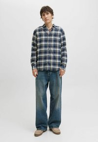 Grovternet flannel skjorte i blå, hvid og creme; knaplukning med lange ærmer. Sættes sammen med brede denim bukser og lysebrune sko.