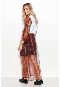 Przezroczysty kwiatowy kimono w czerwieni i brązie z bufkami, nałożone na biały top, charakteryzujące się zwiewnym krojem i czarnymi butami.