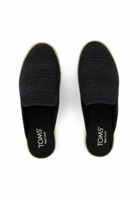 Black slip-on shoes with a textured upper, featuring a woven pattern and light-colored rubber sole. Inside reads "TOMS Wear Good."