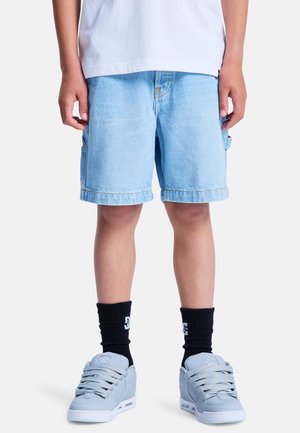 Jasnoniebieskie szorty dżinsowe z podwiniętymi brzegami, bocznymi kieszeniami i żółtym przeszyciem, zestawione z szarymi tenisówkami i czarnymi skarpetkami.