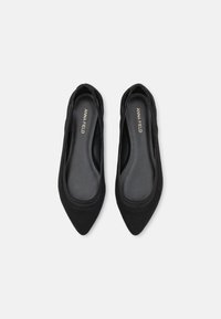 Paire de chaussures plates noires à bouts pointus avec "ANNA FIELD" imprimé sur la semelle intérieure, vues de dessus sur un fond blanc.