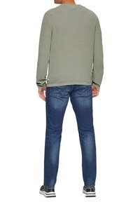 Groene lange mouw trui van gebreid materiaal met een gestructureerde stof, gecombineerd met blauwe denim jeans. De trui heeft een ronde halslijn en subtiele zoomdetails.