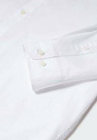 Chemise blanche à boutons avec un poignet replié, dotée de deux boutons beiges et d'une texture lisse. Design simple, sans motifs ni accents.