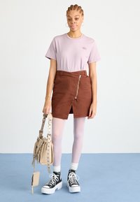 Lys lilla t-skjorte, brun semsket omslagskjørt med glidelås foran, lys rosa strømpebukser, svarte høyhælte sneakers med hvite såler, beige skulderveske.