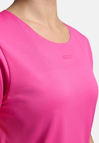 Camiseta deportiva de manga corta y cuello redondo en rosa brillante, con tejido texturizado y transpirable con pequeños orificios y un detalle sutil de logo.