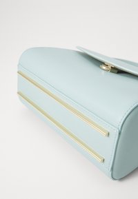Borsa di pelle azzurro chiaro con una texture liscia, caratterizzata da due dettagli in metallo dorato e una chiusura a pattina. Forma arrotondata con dettagli di cucitura ordinati.