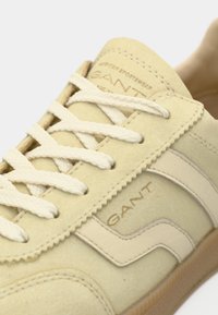 Μπεζ σουέντ αθλητικά παπούτσια με λευκές λεπτομέρειες, υφασμένα κορδόνια και ανάγλυφο λογότυπο. Διαθέτουν χαμηλό προφίλ και κλασικό αθλητικό σχέδιο.