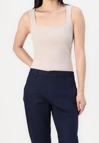 Beżowy top na ramiączkach z kwadratowym dekoltem, zestawiony z granatowymi spodniami. Materiał wydaje się gładki, z dopasowanym krojem i minimalnymi, widocznymi szwami.