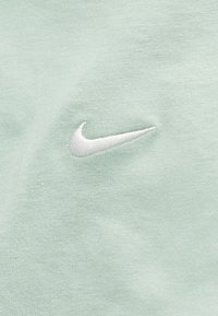 Λευκό λογότυπο Nike swoosh κεντημένο σε ανοιχτό πράσινο ύφασμα, με λεπτομερή πλεκτή υφή.