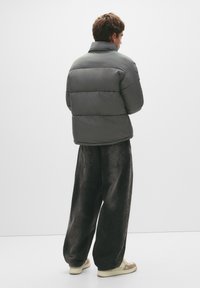 Puffet grå jakke med høj krave, polstret design og quiltet tekstur, parret med løse mørke jeans og lyse sneakers.