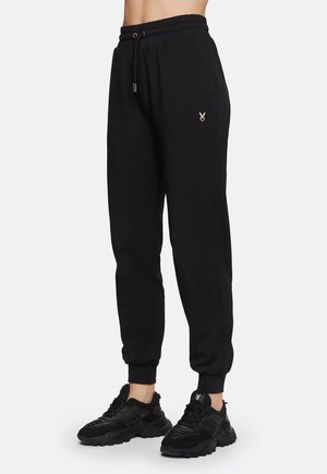 Schwarze Jogginghosen aus Stoff, mit elastischem Bund, seitlichen Taschen und gerippten Bündchen. Ein kleines Logo ist nahe der Hüfte gestickt.