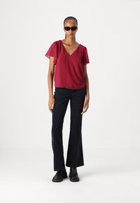 Maroon top with short flutter sleeves and a V-neckline, paired with flared black pants and black chunky boots. Smooth fabric with no patterns.