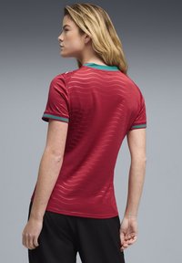 Κόκκινο αθλητικό μπλουζάκι με ανάγλυφο κυματοειδές σχέδιο, γιακά και μανίκια με πράσινες και κόκκινες ρίγες, και εφαρμοστή σχεδίαση.