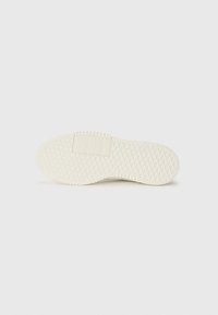Suela de zapato de goma blanca con una superficie texturizada en patrón de diamante y un tacón plano. Presenta un pequeño parche rectangular cerca de la zona del talón.