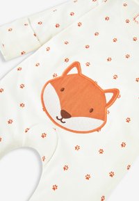 Weicher, cremefarbener Strampler mit einem Applikation eines orangefarbenen Fuchsgesichts und verstreuten kleinen Pfotenabdruckmustern in Orange. Hergestellt aus leichtem Baumwollmaterial.