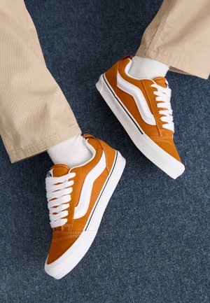 Sneakers in tela arancione con accenti bianchi e design con lacci, dotati di una superficie testurizzata e suola in gomma bianca a profilo basso.
