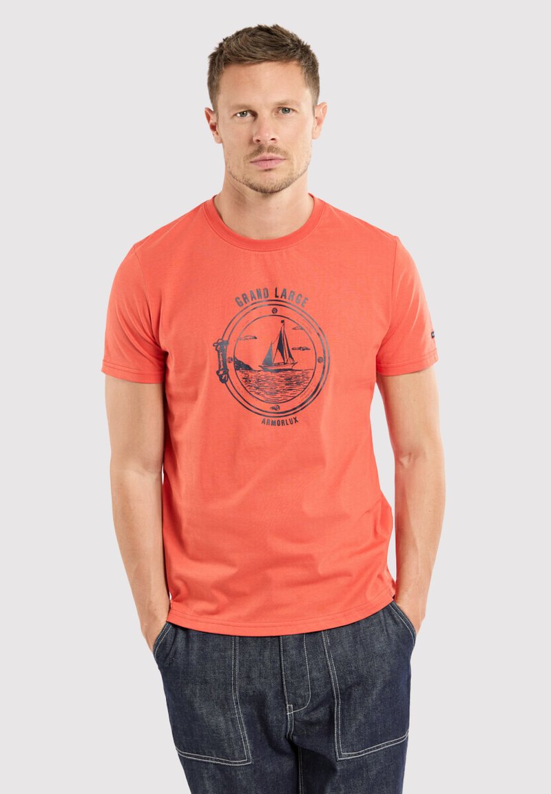 T-shirt en coton orange avec un col rond et des manches courtes, présentant un graphique de voilier bleu foncé et du texte sur le devant.