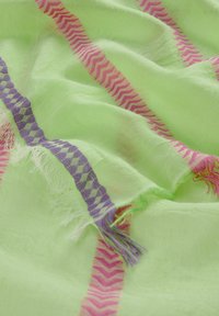 Tissu vert clair avec des rayures en zigzag roses et violettes. Texture douce avec des bords effilochés. Matériau léger et transparent.